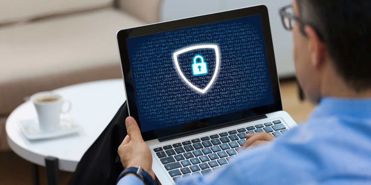 Mann arbeitet am Laptop, auf dem Bildschirm ein Symbol für Datenschutz – ein digitales Sicherheitsschloss